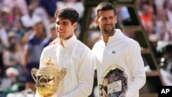 Carlos Alcaraz of Spain holds his trophy as he stands with Novak Djokovic of Serbia after winning the men's singles final at the Wimbledon tennis championships in London, July 14, 2024. 