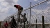 Migrantes que cruzaron el Río Grande desde México hacia Estados Unidos trepan una valla con alambre de púas, el lunes 21 de agosto de 2023, en Eagle Pass, Texas.