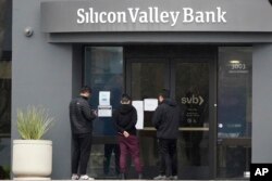 FILE - People look at signs posted outside of an entrance to Silicon Valley Bank after the bank suddenly shut down, in Santa Clara, California, March 10, 2023.