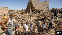 Para relawan menyaksikan penggali memindahkan puing-puing rumah yang runtuh di Tafeghaghte, barat daya Marrakesh, Minggu 10 September 2023, dua hari setelah gempa bumi berkekuatan 6,8 skala Richter melanda kawasan itu.