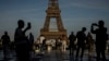 FILE - People use their smartphones near the Olympic rings displayed on the Eiffel Tower in Paris, June 7, 2024.