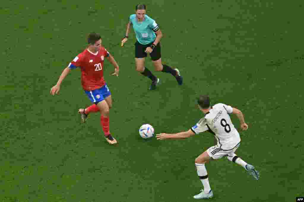 Mobeti piololo ya mwasi ya ekolo France Stephanie Frappart (C) azali kotala milieu ya Costa Rica #20 Brandon Aguilera (G) kowelela ndembo na milieu ya Allemgane #08 Leon Goretzka na Mondial Qatar 2022 na stade Al-Bayt, Doha, 1er décembre 2022. (Photo Fran