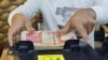 FILE - A man counts Iraqi dinars on a money counting machine at a currency exchange shop in Baghdad, Iraq, Jan. 23, 2023. 