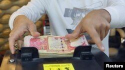 FILE - A man counts Iraqi dinars on a money counting machine at a currency exchange shop in Baghdad, Iraq, Jan. 23, 2023. 