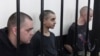 Двоє громадян Великобританії Ейден Аслін (ліворуч) і Шон Піннер (праворуч) і марокканець Саудун Брагім (в центрі) сидять за ґратами в залі суду в Донецьку, на території, що підконтрольна уряду ДНР, на сході України, четвер, 9 червня 2022 р. (AP Photo)