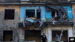 Sejumlah warga berdiri di balkon apartemen mereka yang rusak akibat gempuran rudal Rusia di Dobropillya, Wilayah Donetsk, timur Ukraine, Sabtu, 30 April 2022. (Foto: Evgeniy Maloletka/AP Photo)