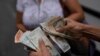 Un trabajador de un autobús público cuenta bolívares venezolanos y dólares estadounidenses, mientras da cambio para un pasajero, en el barrio Quinta Crespo de Caracas, Venezuela, el miércoles 9 de agosto de 2023