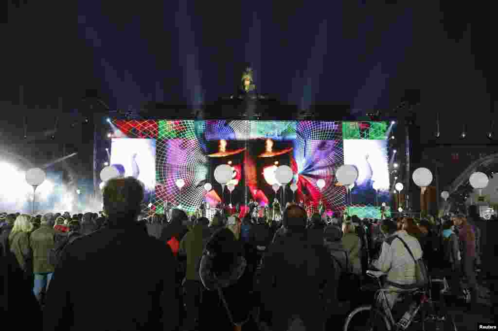 Passersby listen to a soundcheck on stage in front of the Brandenburg Gate before a remembrance of 25 years since the fall of the Berlin Wall, Berlin, Nov. 7, 2014.