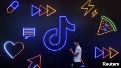 资料照片：在浙江杭州，一名男子持手机走过抖音/TikTok的标识。 (2019年10月18日)