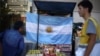 Ciudadanos caminan por las calles de Buenos Aires, frente a una bandera argentina expuesta en un puesto callejero, el 12 de diciembre de 2023.