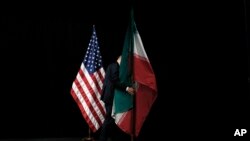 Seorang petugas membereskan bendera Iran yang terpasang di samping bendera AS dari atas panggung setelah pembicaraan nuklir Iran selesai dilaksanakan di Wina, Austria, pada 14 Juli 2015. (AP/Carlos Barria)