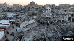 Warga Palestina berjalan di antara puing-puing bangunan, di tengah gencatan senjata antara Israel dan Hamas, di Khan Younis, di Jalur Gaza selatan, 27 Februari 2025. (Foto: Ramadan Abed/Reuters)